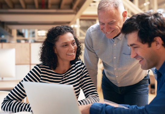 A woman and two men smile as they look at traditional and digital marketing strategies for nonprofit fundraising on a laptop.